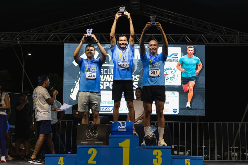 Pódio masculino dos 5 km: troféus ao alto sob as luzes do palco.